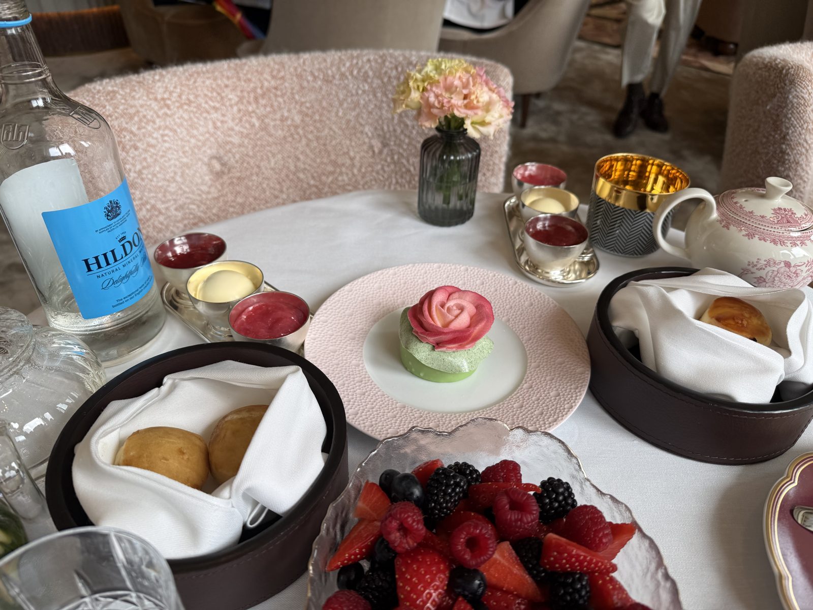 Complimentary patisserie — pink sugar rose on pistachio dome — alongside gluten-free scones, clotted cream, jam and berries